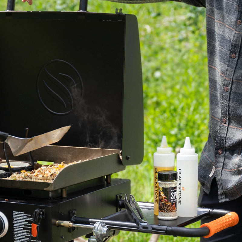 Blackstone 2350 22 inch On The Go Omnivore FlexFold Griddle with oils on the side table