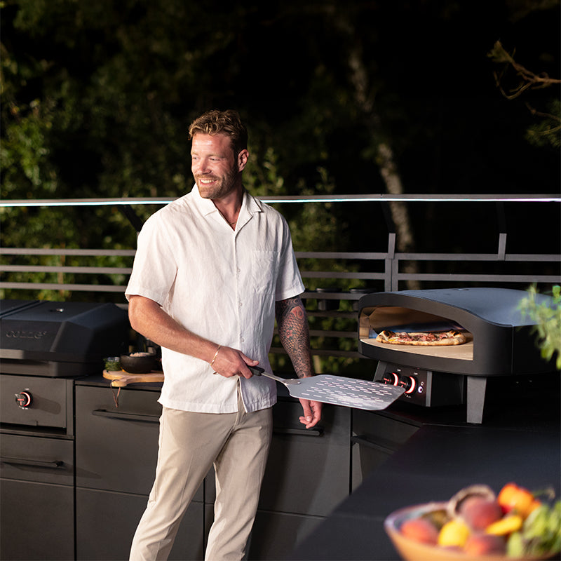 Cozze 24inch Black Edition Gas Pizza Oven cooking pizza outside with pizza padel