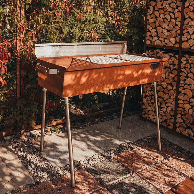 GrillSymbol Charcoal Grill Naked Chef XXL outside on tiles next to firewood racks
