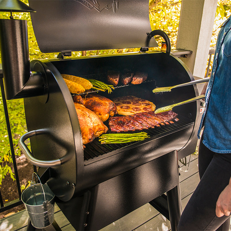 A black Traeger Pro575 outdoor pellet grill with the lid open, showing cooked food on the grates. 