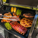Close up of a black Traeger Pro575 outdoor pellet grill with the lid open, showing cooked food on the grates. 