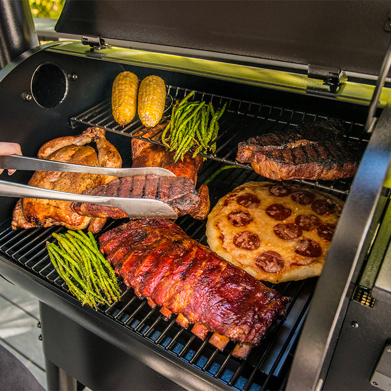 Close up of a black Traeger Pro575 outdoor pellet grill with the lid open, showing cooked food on the grates. 