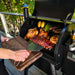 Traeger Pro575 Black international with hood open, removing food from the grill.